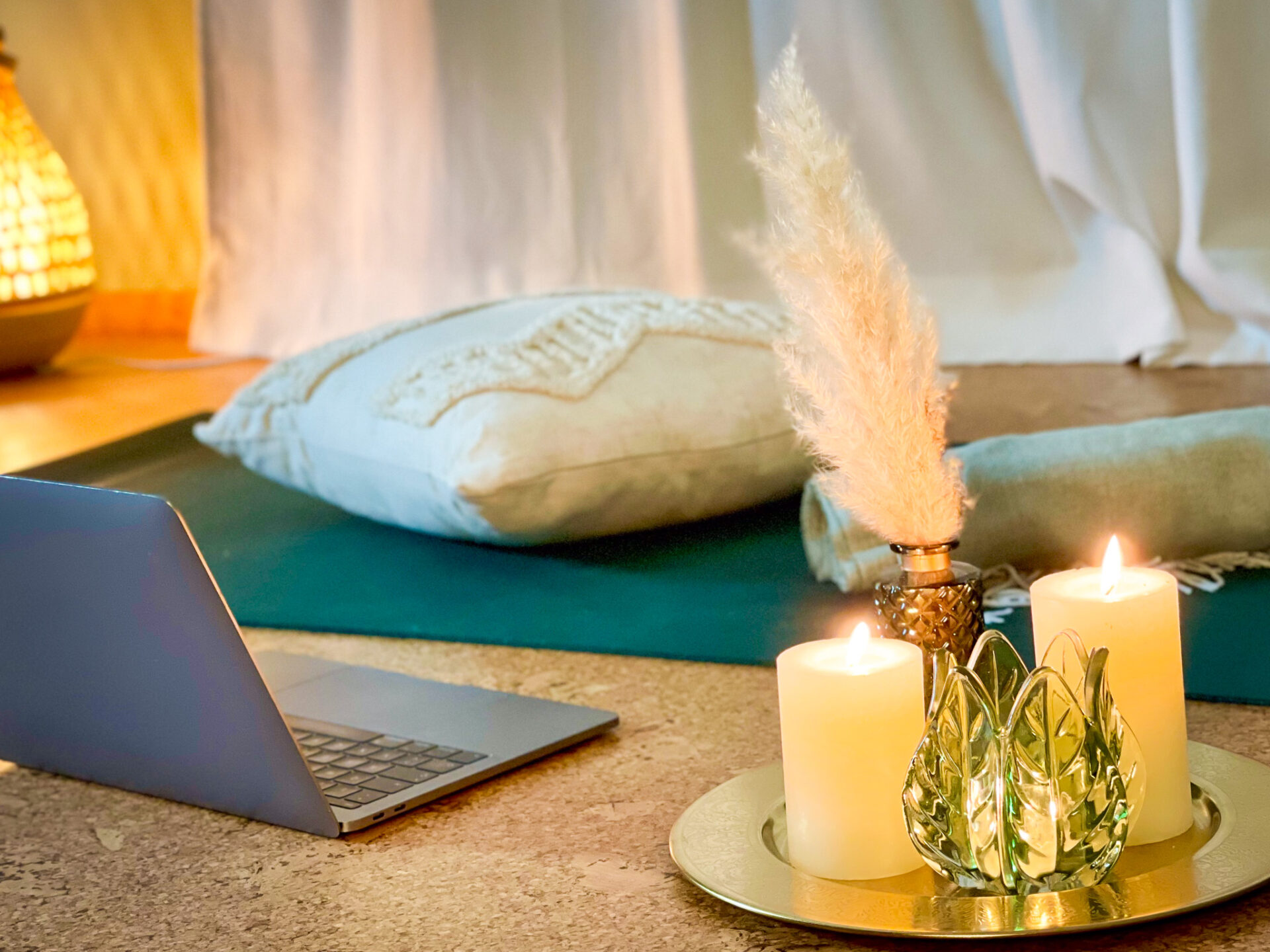 Vor einem Laptop liegen eine Yogamatte sowie eine Decke und ein Kissen für eine entspannte Online Yogastunde parat